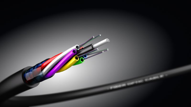 Close-up of a fiber optic cable with exposed colored wires and filaments against a dark, blurred backdrop.