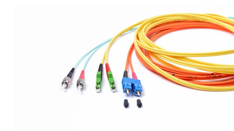 Colorful fiber optic cables with various connectors are arranged on a white background.
