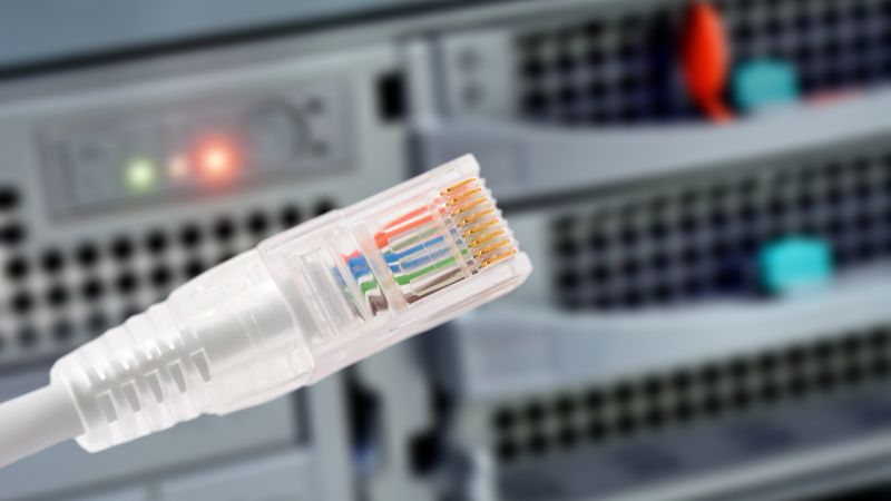 Ethernet cable close-up with blurred server equipment and indicator lights in a data center.